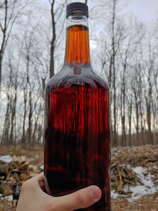 hand holding up bottle of maple syrup from Garside Gardens