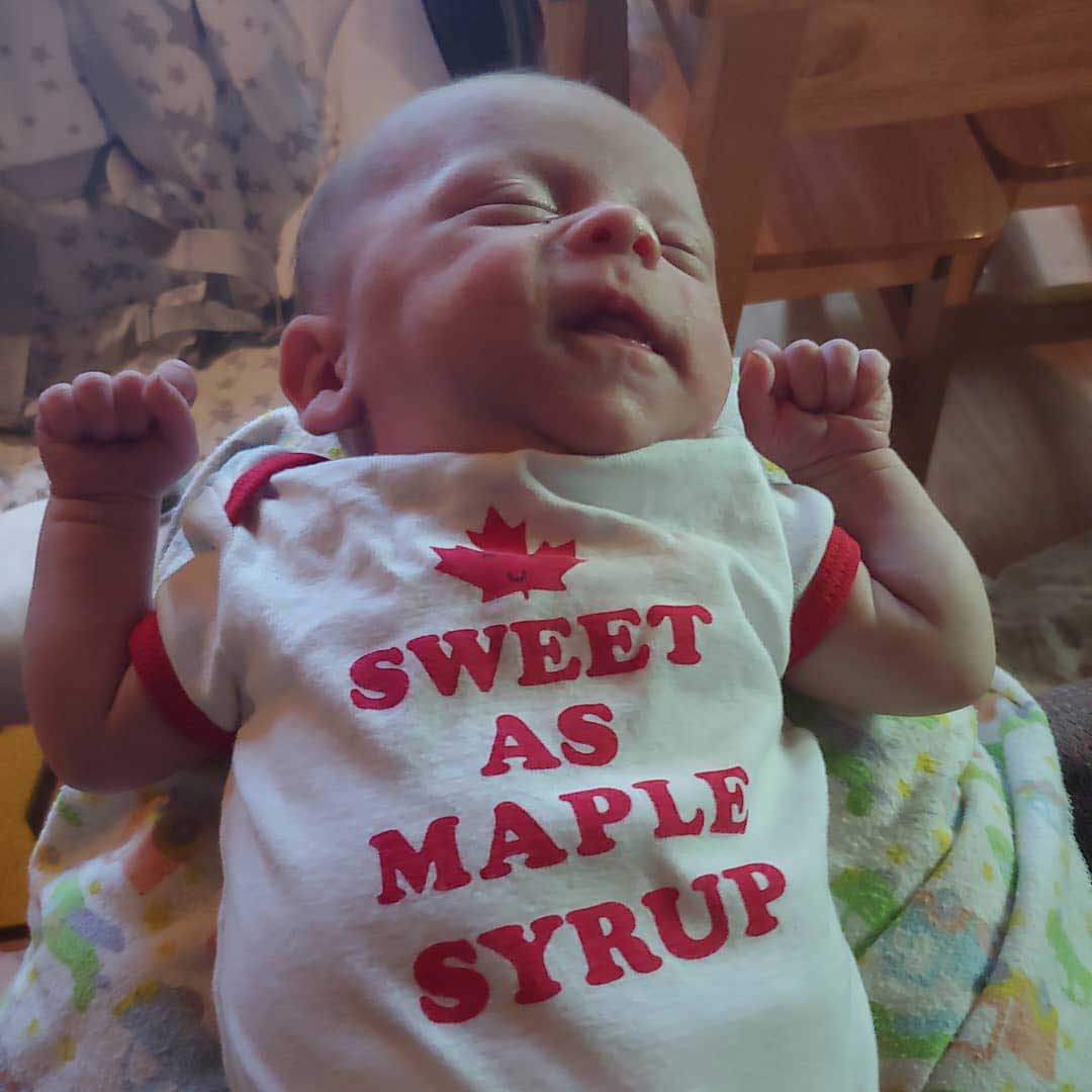 photo of a newborn baby wearing a white shirt that says sweet as maple syrup