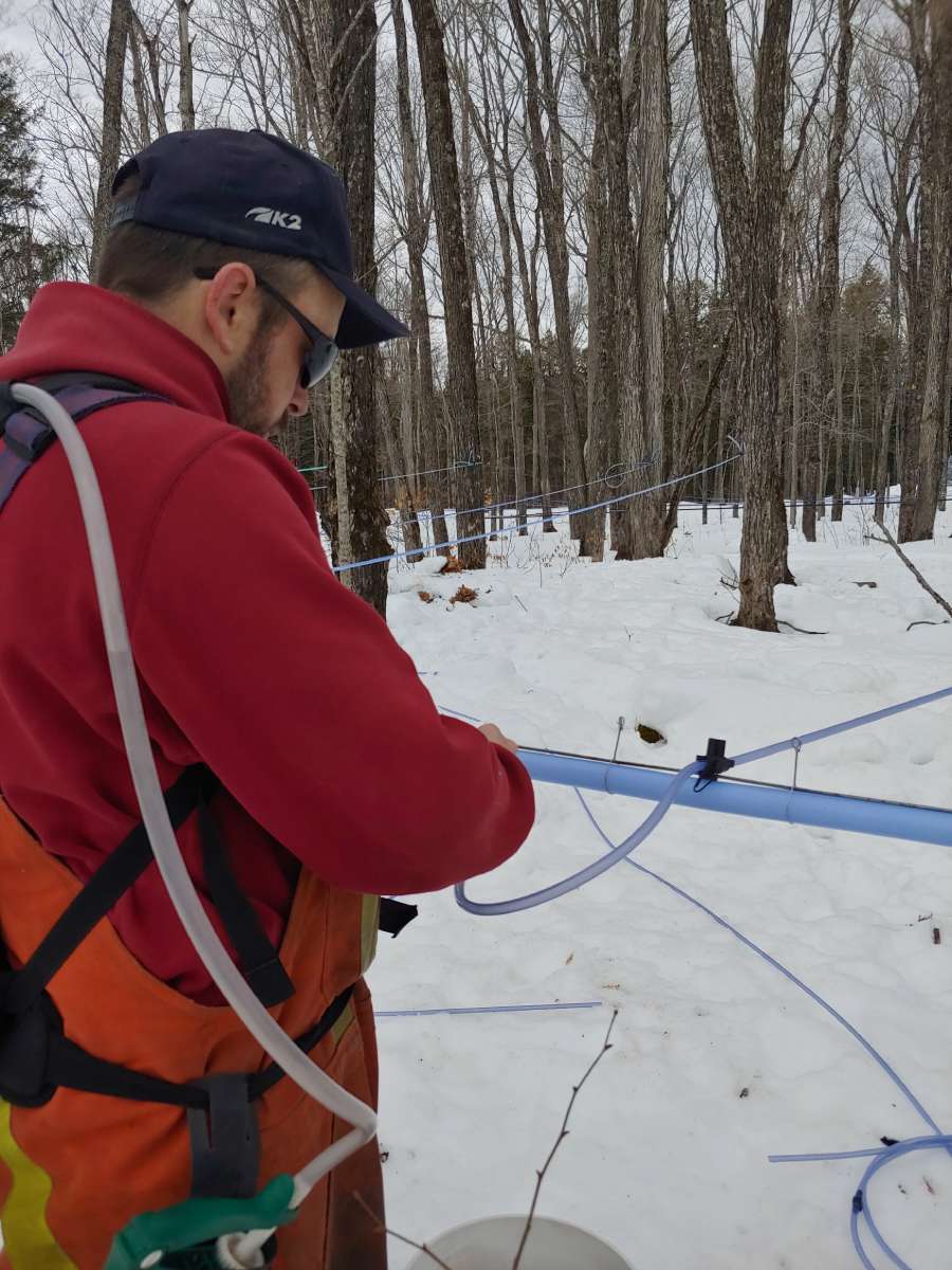 man checking syrup lines outside with snow on ground
